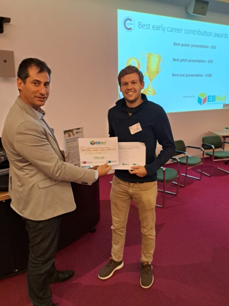 Two men stand holding certificates smiling the the camera.