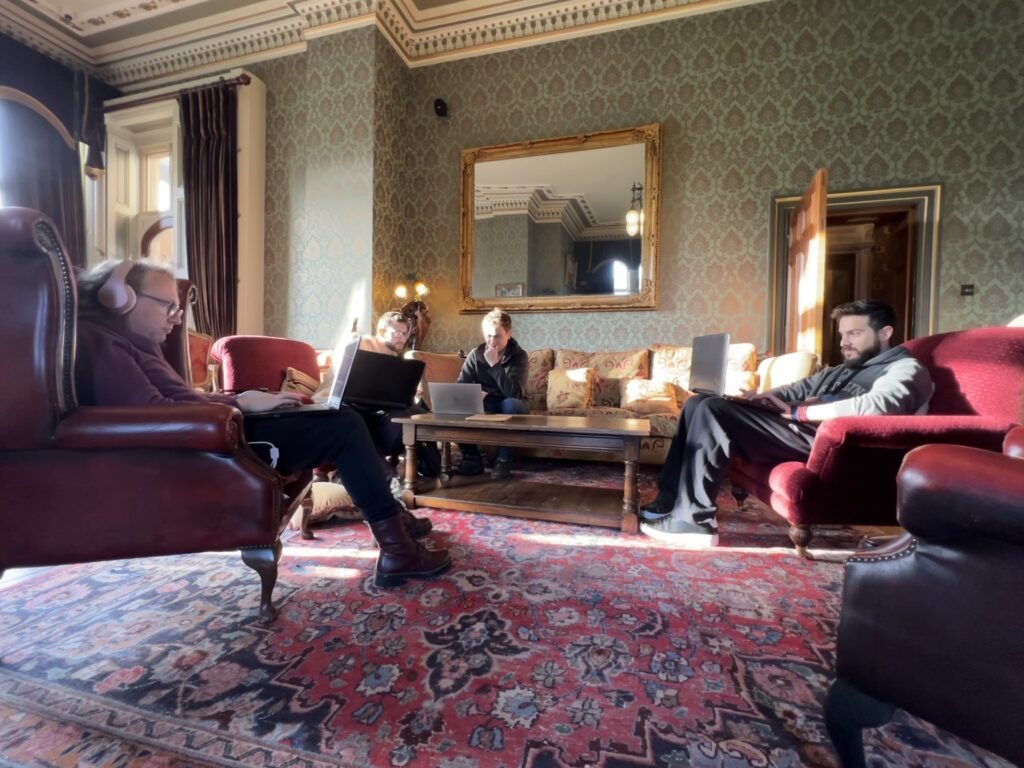 Several people sit on ornate chairs in a stately room. they are working on laptops