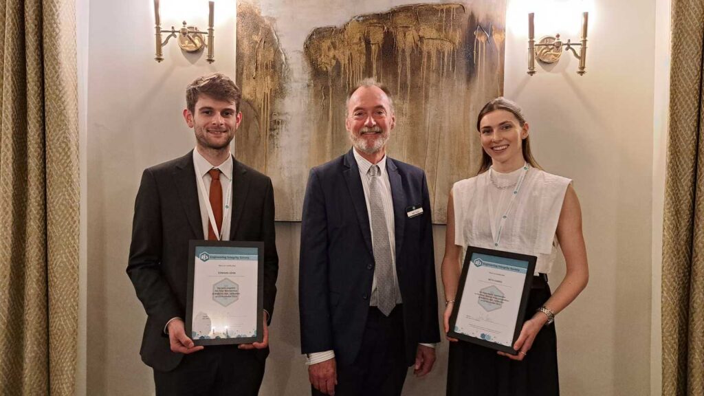 Edward John stands to the left of two other people. all are wearing smart clothes and smiling at the camera. the two outer people are holding certificates