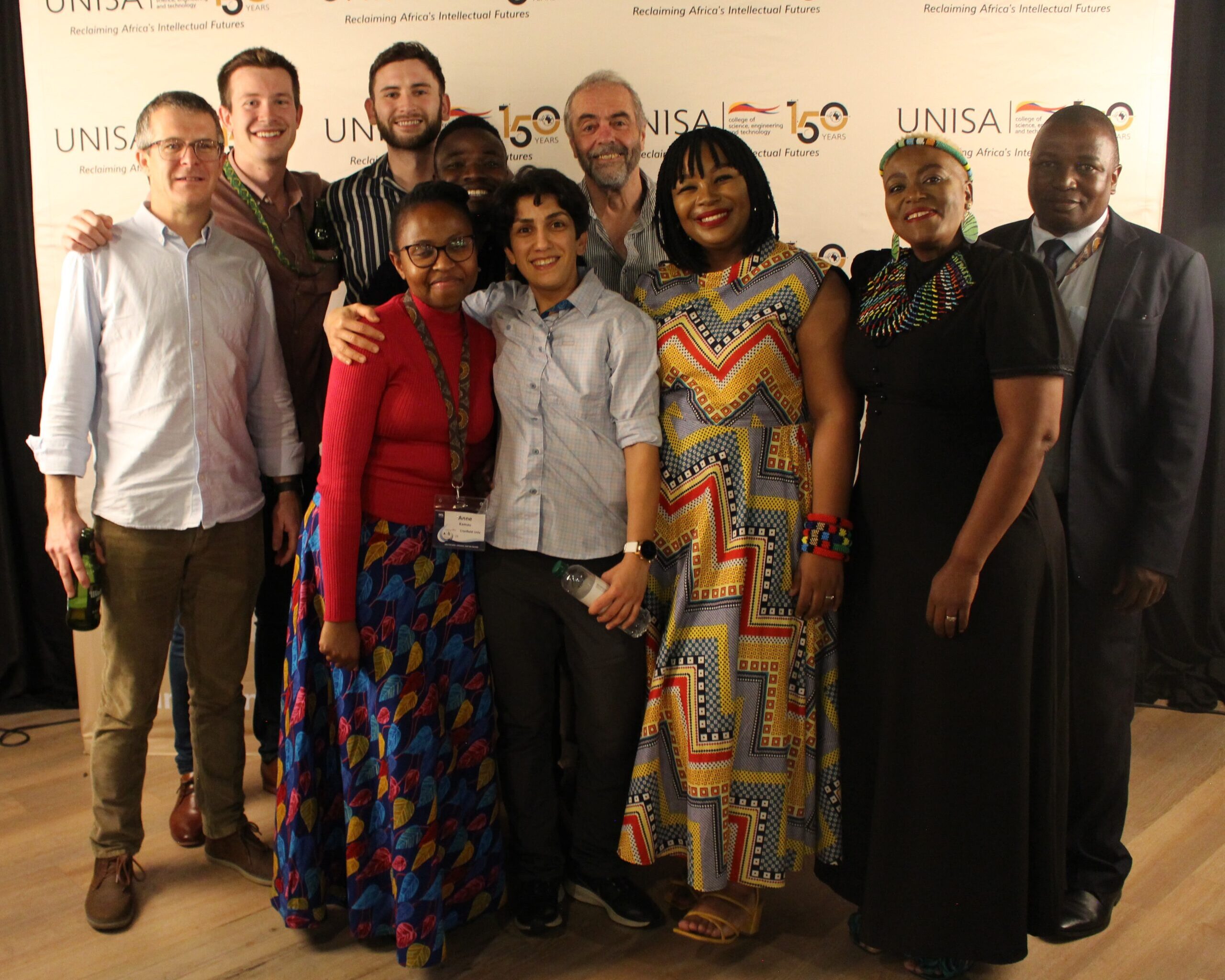 A group of people stand smiling at the camera, some have their arms around each other.