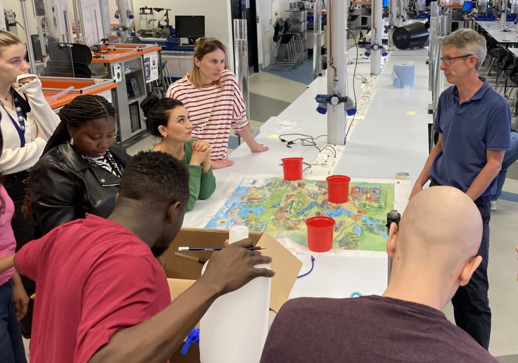 A group of WIRe PhD students gathered around a lab bench listening to a presenter. On the bench is a map and some red cups.