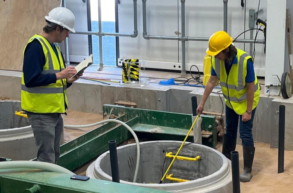 Two WIRe students wearing hard hats and high-vis vests looking at a large pipe