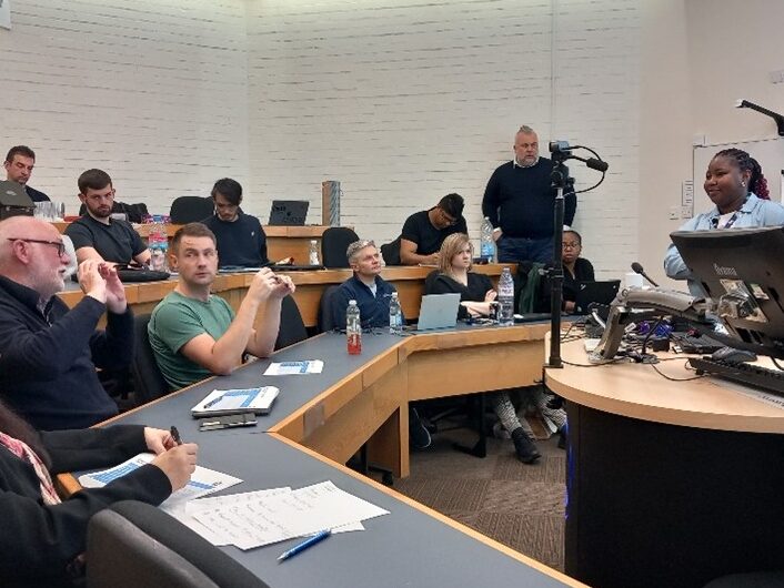 A group of WIRe staff and PhD students in a lecture theatre, one student is presenting to the room