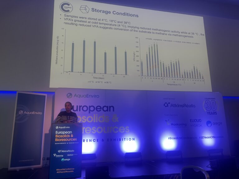 A woman presents behind a lectern, with a project screen behind her showing a slide titles 'storage conditions'