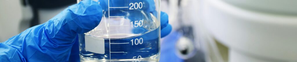 hand in a blue rubber glove holding a glass beaker of water
