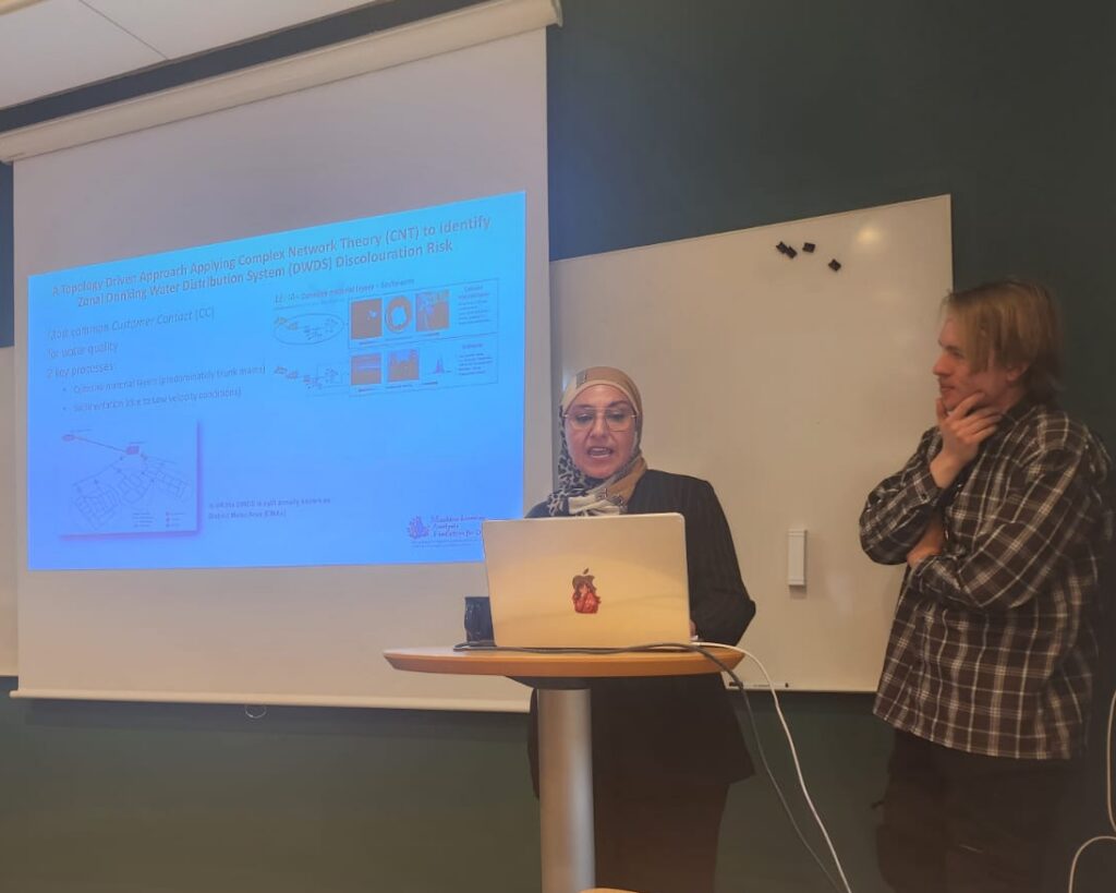 a woman and a man stand next to a projector screen