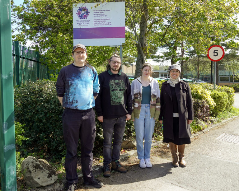 A group of 4 people stand in a line smiling at the camera. Above them is a sign that reads 'Westborough High School'