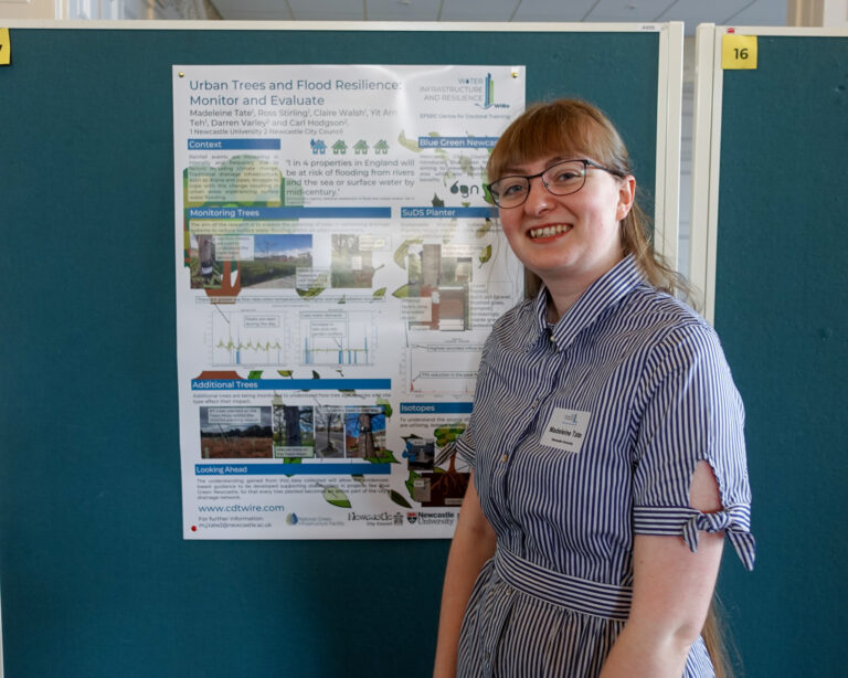 A woman stands smiling next to a scientific poster
