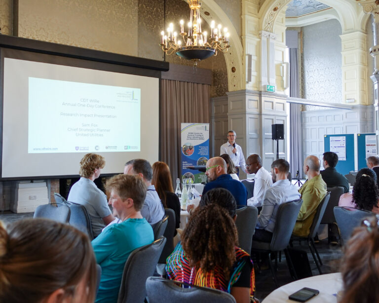 A man presents to a room full of people sat at round tables