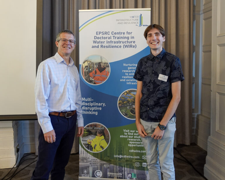 two men stand smiling at the camera. between them is a roller banner promoting CDT WIRe