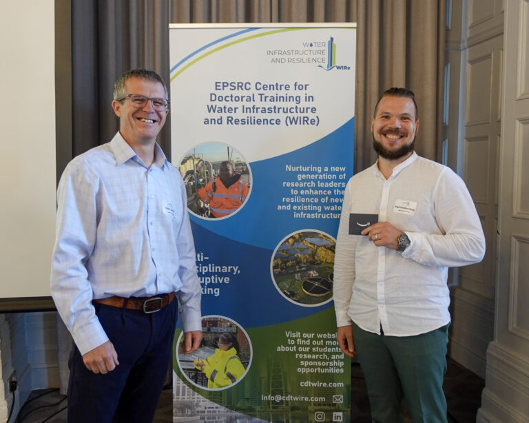 two men stand smiling at the camera. between them is a roller banner promoting CDT WIRe