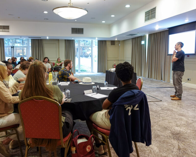 A man presents to a room of people sat at round tables