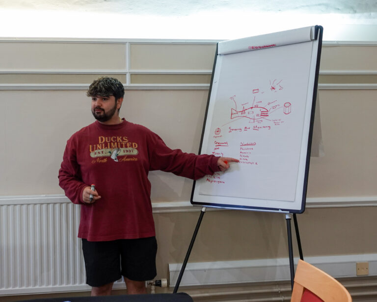 a man stands next to a flipchart with a diagram of a robot in the shape of a whale