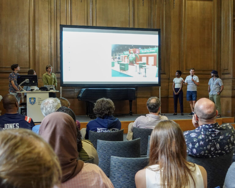a group of people stand beside a projector screen, presenting to an audience