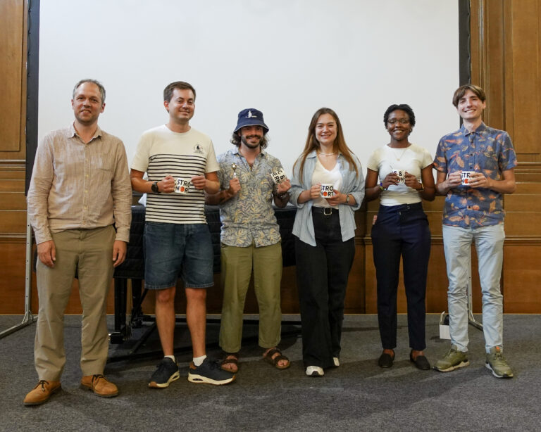 six people stand in a row smiling at the camera, they are each holding a mug and teaspoon