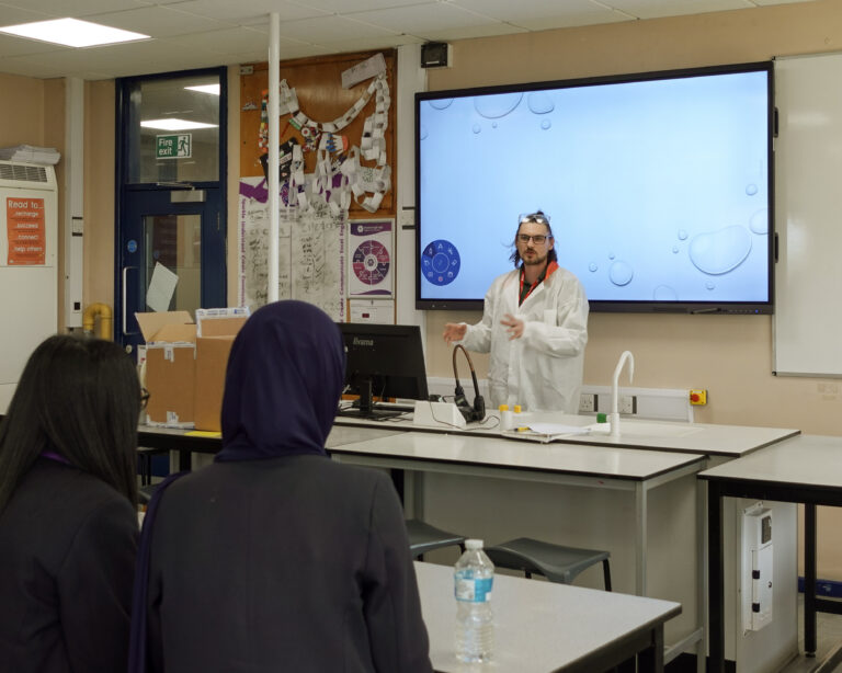 a man wearing a lab coat addresses a classroom of children