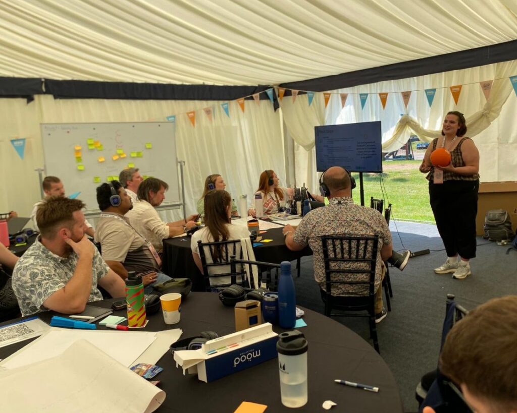 a woman delivers a presentation to a group of people sat in a marquee