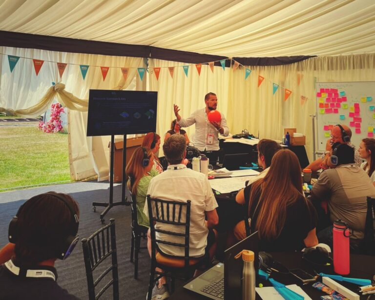 a man delivers a presentation to a group of people sat in a marquee