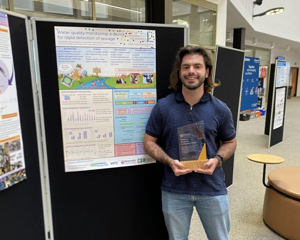 A man stands next to a scientific poster holding a glass trophy