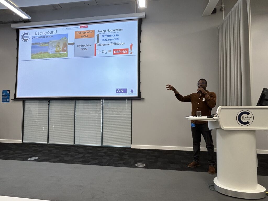 A man presents with a projector screen beside him