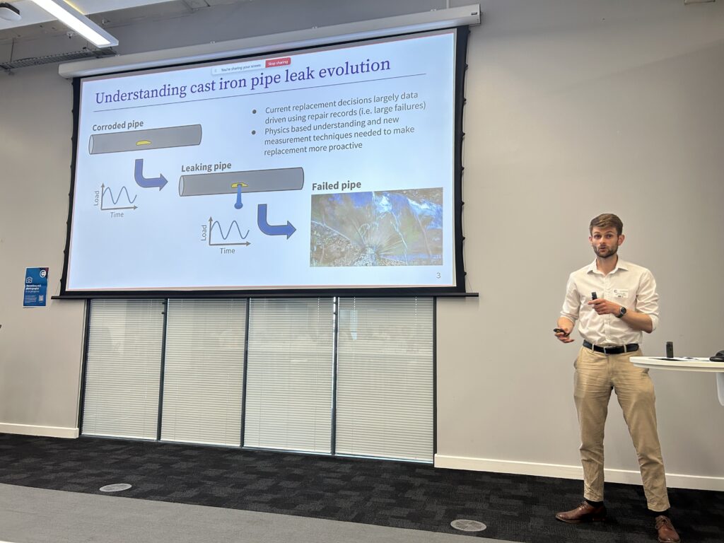 A man presents with a projector screen beside him